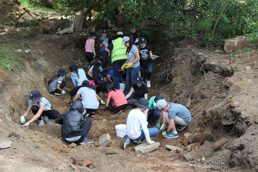 School children sit in dirt hole digging