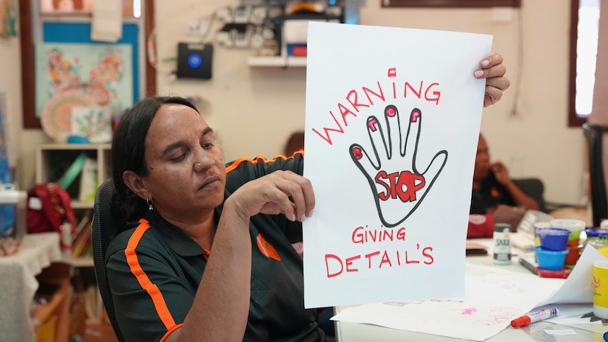 A woman holds up a hand-painted sign saying Stop giving details.