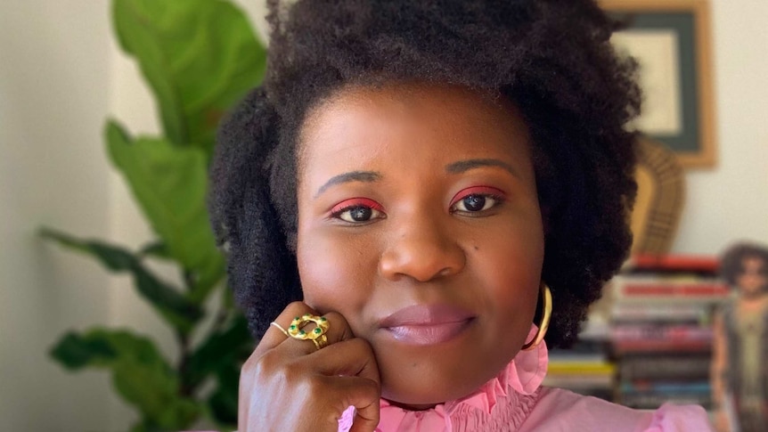 A woman in a pink ruffled top smiling to camera.