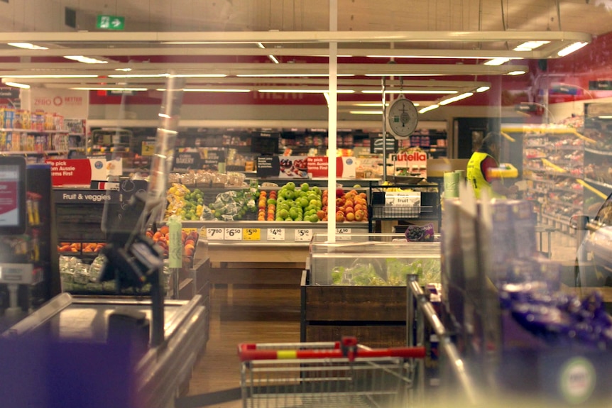Mirando a través del cristal un supermercado Coles casi vacío.  Las cajas se pueden ver delante de frutas y verduras.