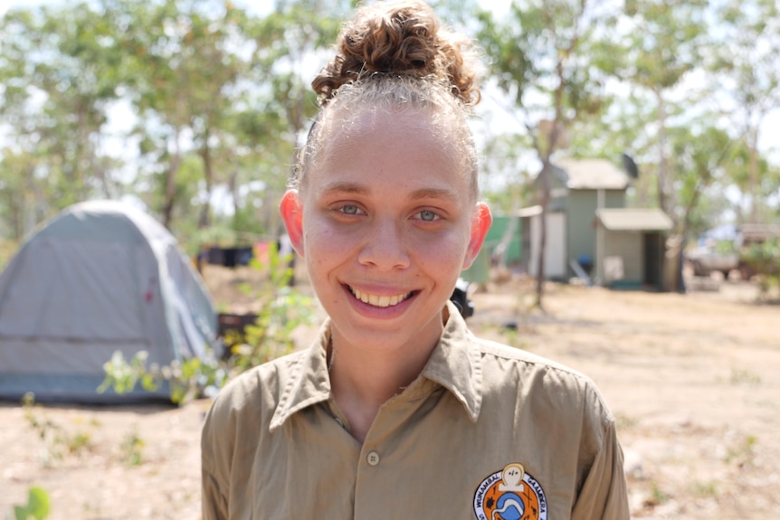 indigenous woman smiles to camera with bush and tents in background