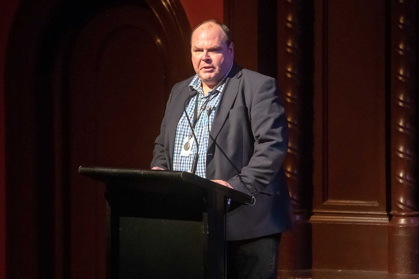 A man stands at a podium and speaks to an audience