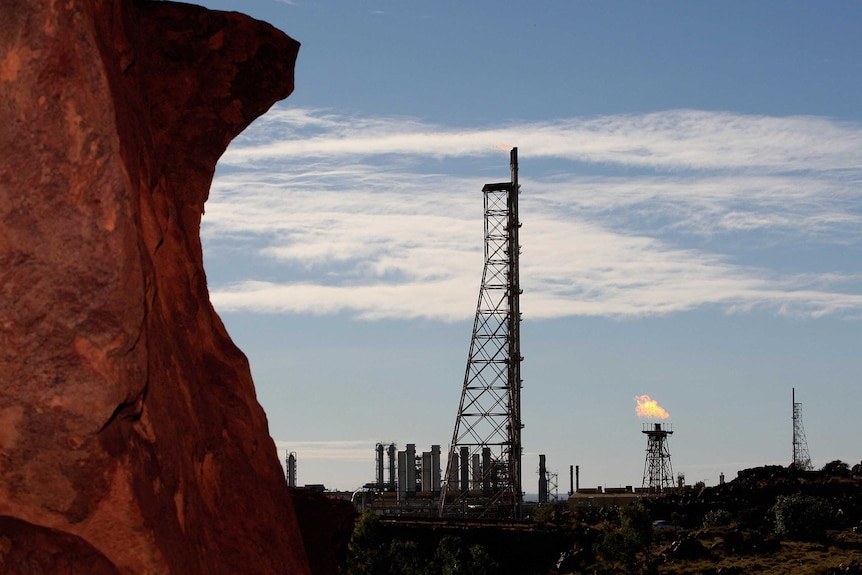 A rust-coloured rocky outcrop on the left of the image stands in stark contrast to a gas field in the middle distance 