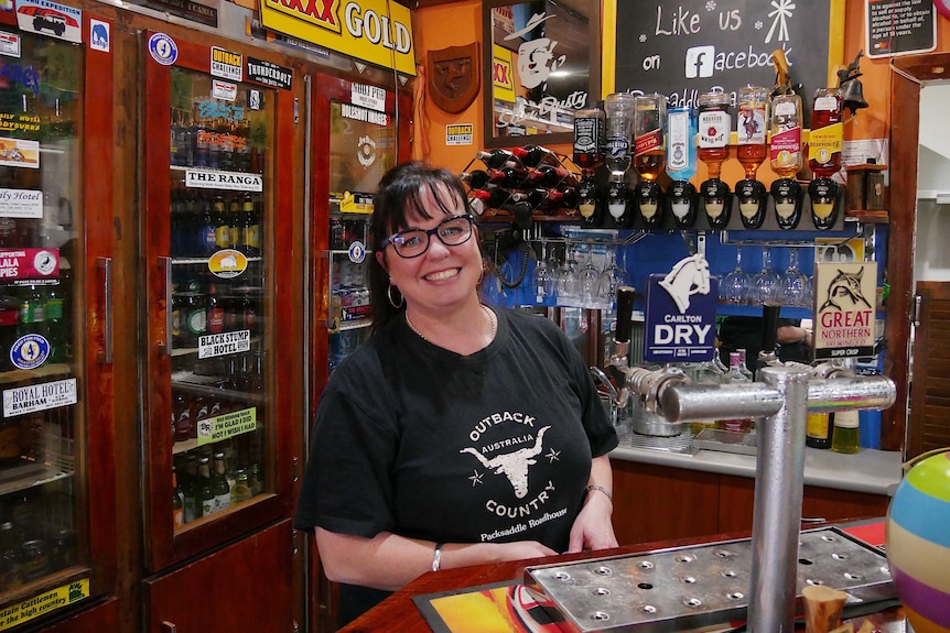 A smiling, dark-haired woman standing behind a bar.