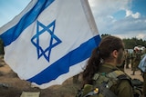 A female Israeli soldier holds an Israeli flag.