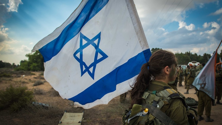 A female Israeli soldier holds an Israeli flag.