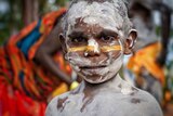 A young aboriginal boy painted in white and yellow body paint stares into the camera.
