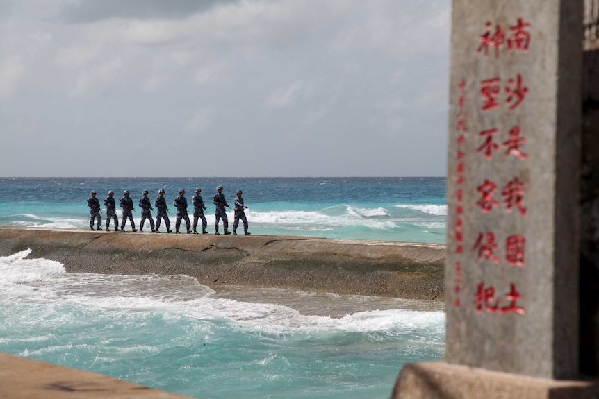 Chinese soldiers patrol in the Spratly Islands, near a sign saying the land is 