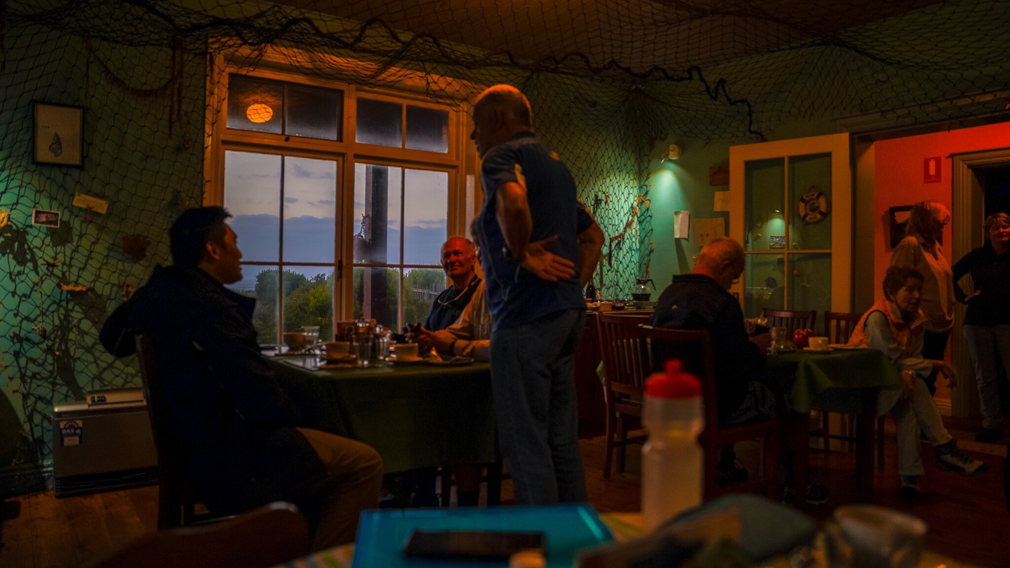 Three men sitting at a table in a dimly lit dining area talk to each other.
