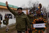 Indian paramilitary officers in green uniforms march and hold floral wreaths for fallen colleagues outside
