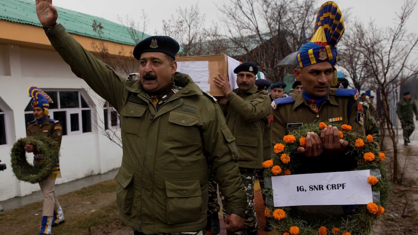 Indian paramilitary officers in green uniforms march and hold floral wreaths for fallen colleagues outside