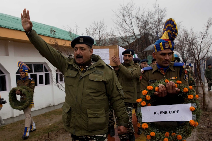 Indian paramilitary officers in green uniforms march and hold floral wreaths for fallen colleagues outside