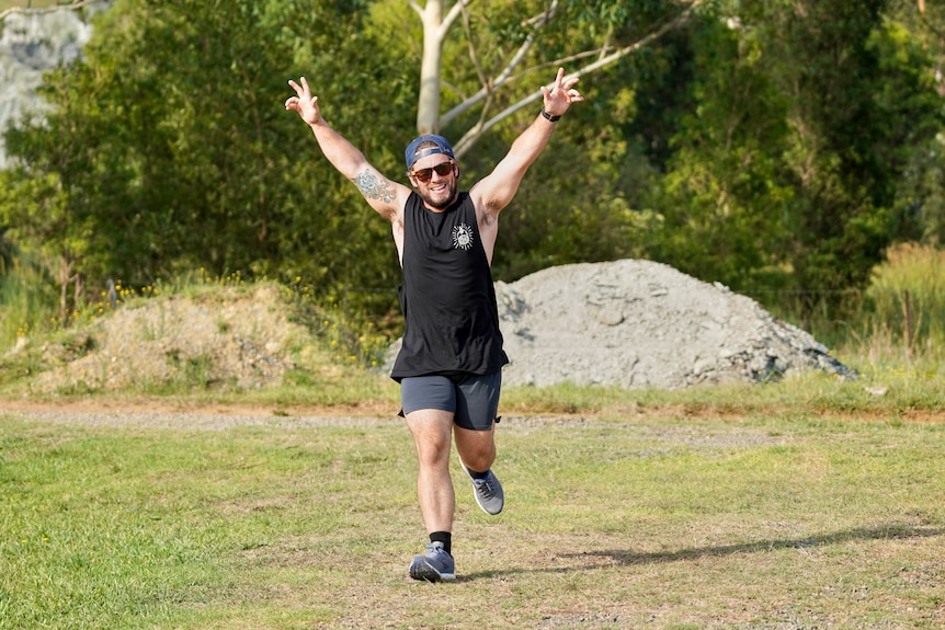 A man lifts his arms in the air to signify he's having a good time, while running at parkrun.