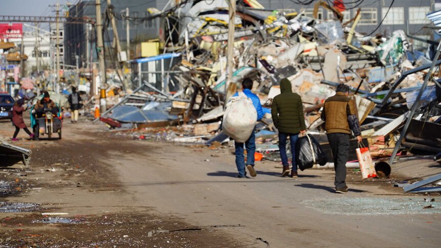 Three migrant workers carry bags and walk away from the demolished Xinjian village.