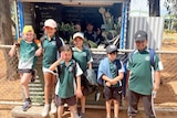 A group of kids wearing green standing in front of a food stand. 