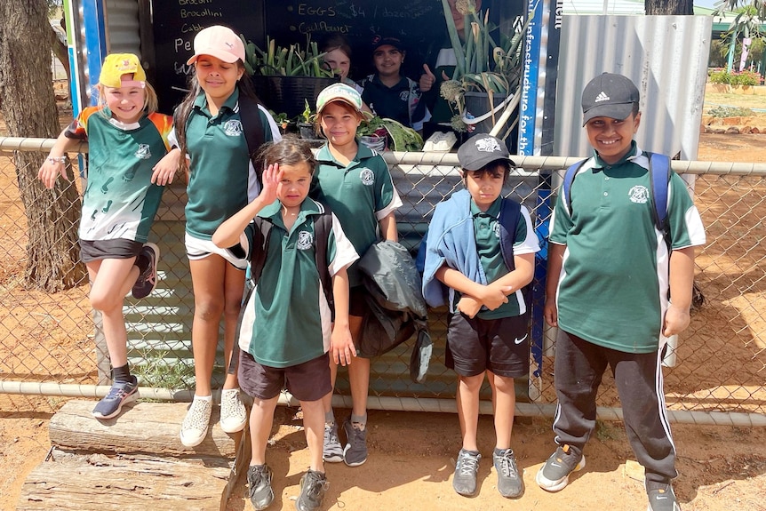 A group of kids wearing green standing in front of a food stand. 