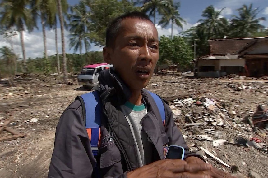 An Indonesian man standing in front of wreckage from a tsunami.