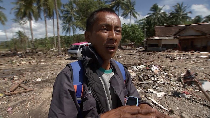 An Indonesian man standing in front of wreckage from a tsunami.