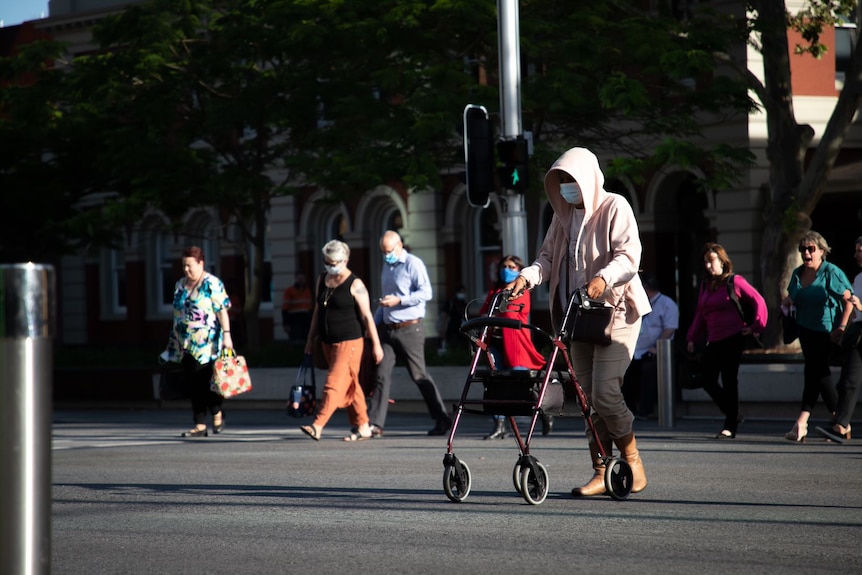 A woman pushing a walking frame crosses a city street.