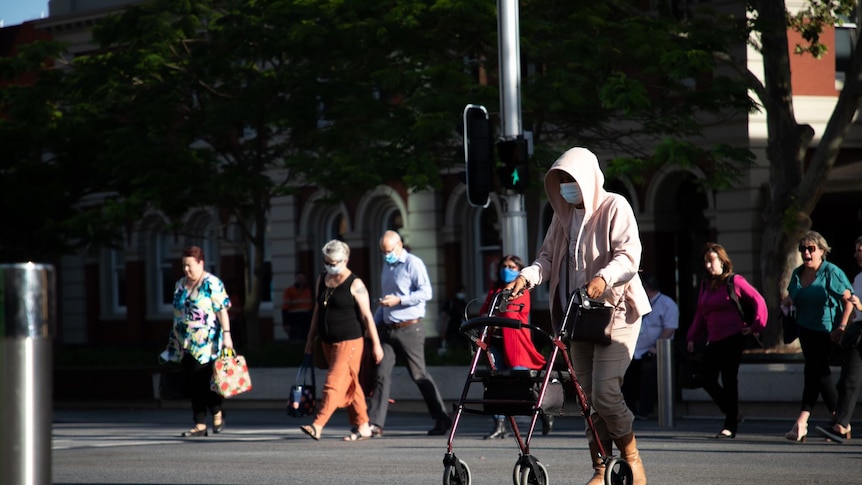 A woman pushing a walking frame crosses a city street.