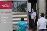 A man in a mask talking to two officials as he stands in the doorway of a Ghan carriage.