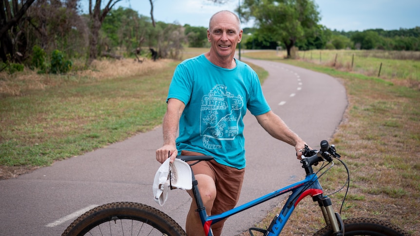 Man standing beside bike on a bike path through a park.