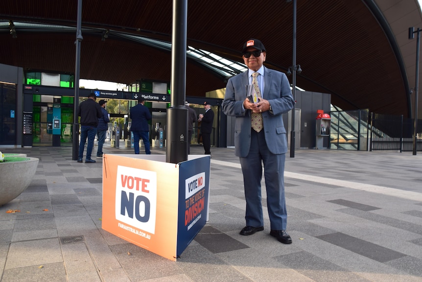 A man stands next to a vote No sign