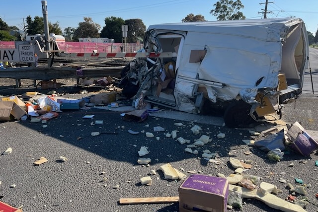 A smashed up van rests beside a level crossing and a boom gate.