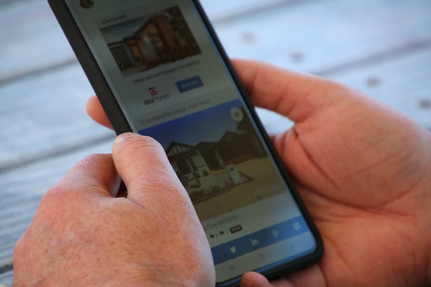 A close-up shot of hands holding a mobile phone with real estate listings on the screen.