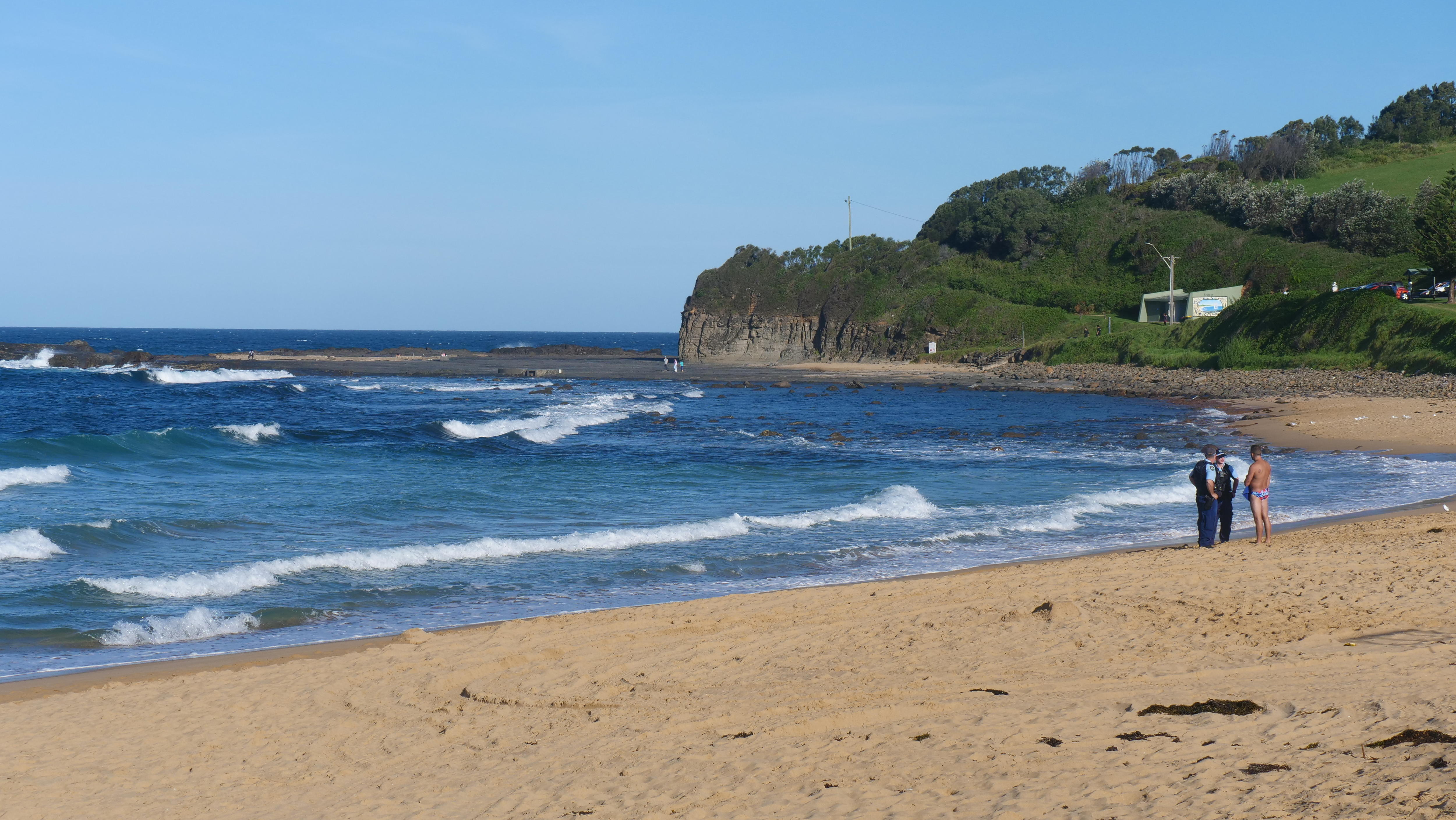A beach, with police officers and a bystander.