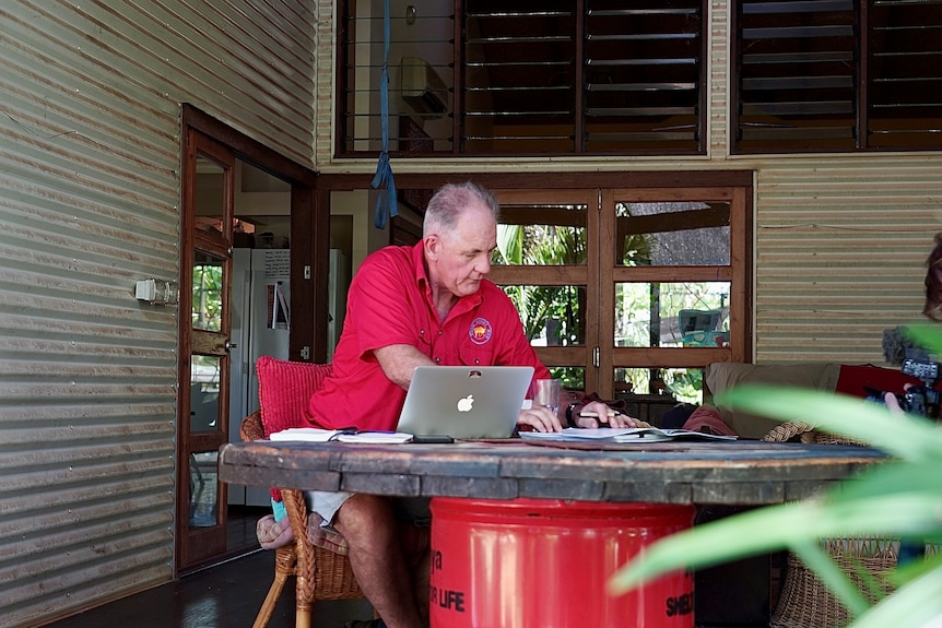 Alan Gray sits outside a corrugated iron house and works on a laptop.
