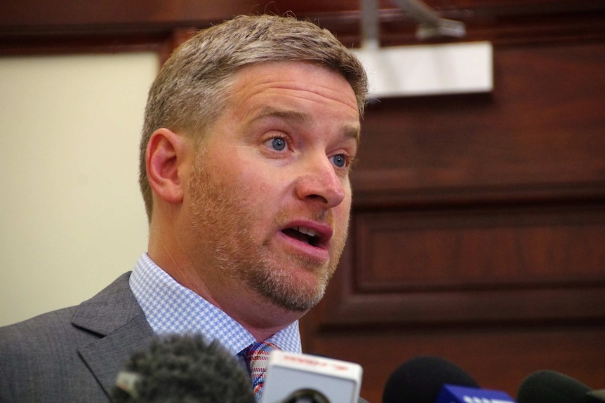 A tight head shot of Brendon Grylls speaking into microphones at a media conference.