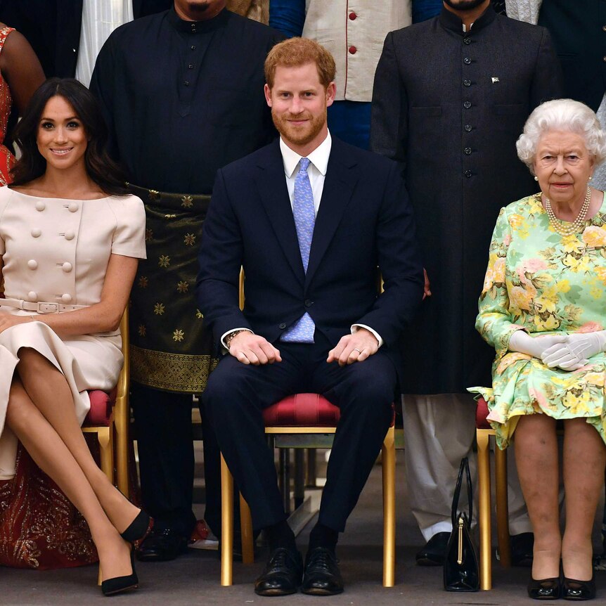 Meghan, Duchess of Sussex, Prince Harry and Queen Elizabeth sit on chairs in front of other people