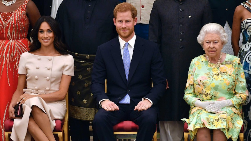 Meghan, Duchess of Sussex, Prince Harry and Queen Elizabeth sit on chairs in front of other people