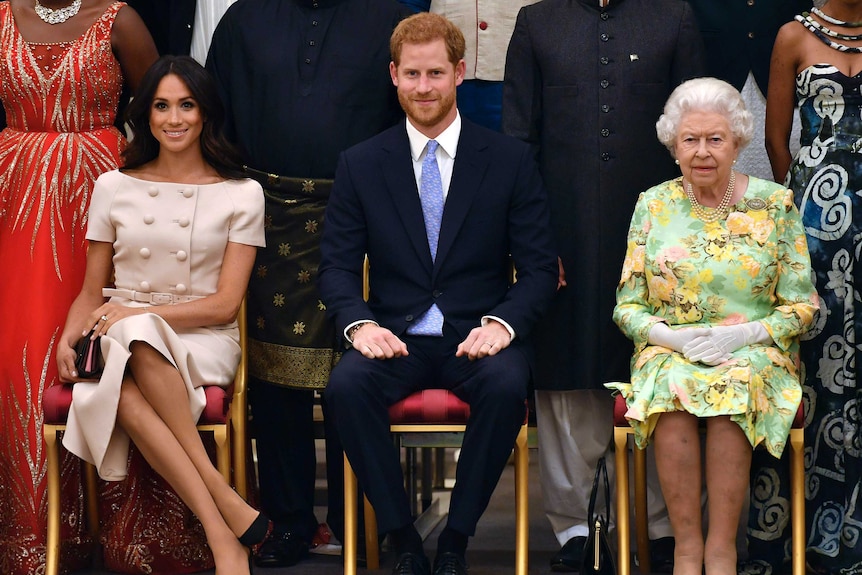 Meghan, Duchess of Sussex, Prince Harry and Queen Elizabeth sit on chairs in front of other people