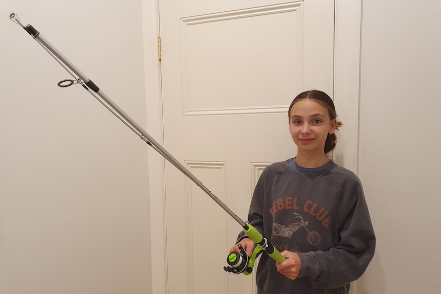 Jess poses with her fishing rod in her suburban Melbourne home