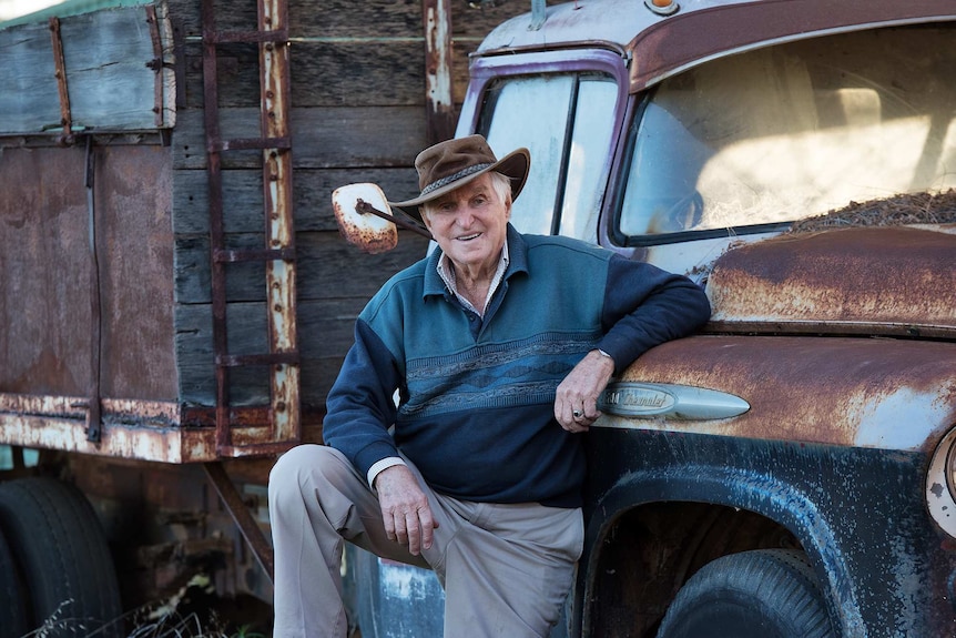 Norman Simon leaning against a Chev truck that has rusted out after years out in the weather.