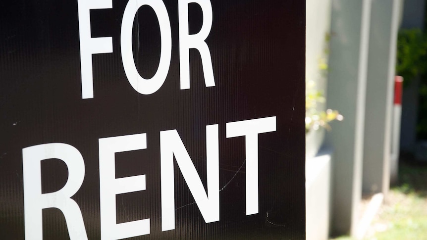 A black and white 'For Rent' sign displayed outside a block of apartments.