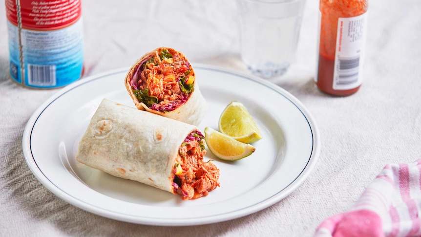 Chicken tinga burrito with kale and corn slaw cut in half and on a plate with lime, a family friendly Mexican dinner recipe.