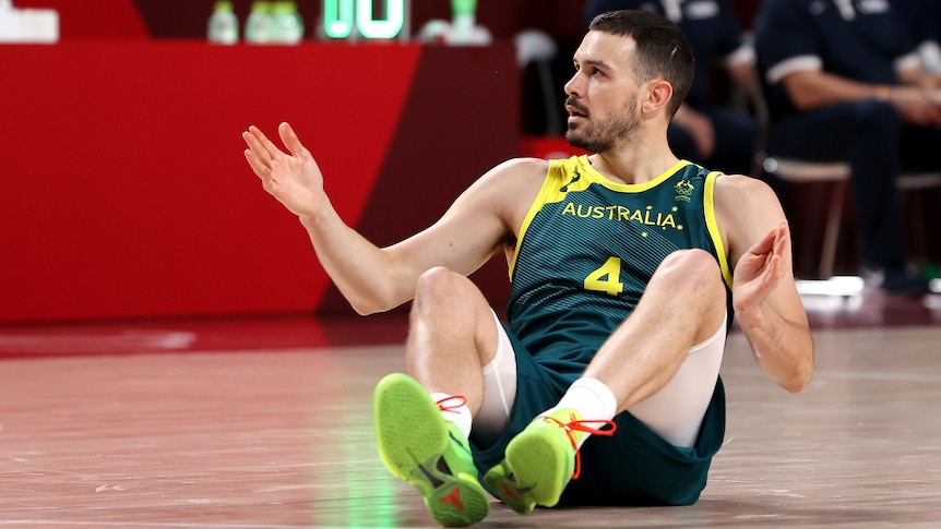 An Australian male basketballer sits on the boards during their Tokyo Olympics game against USA.