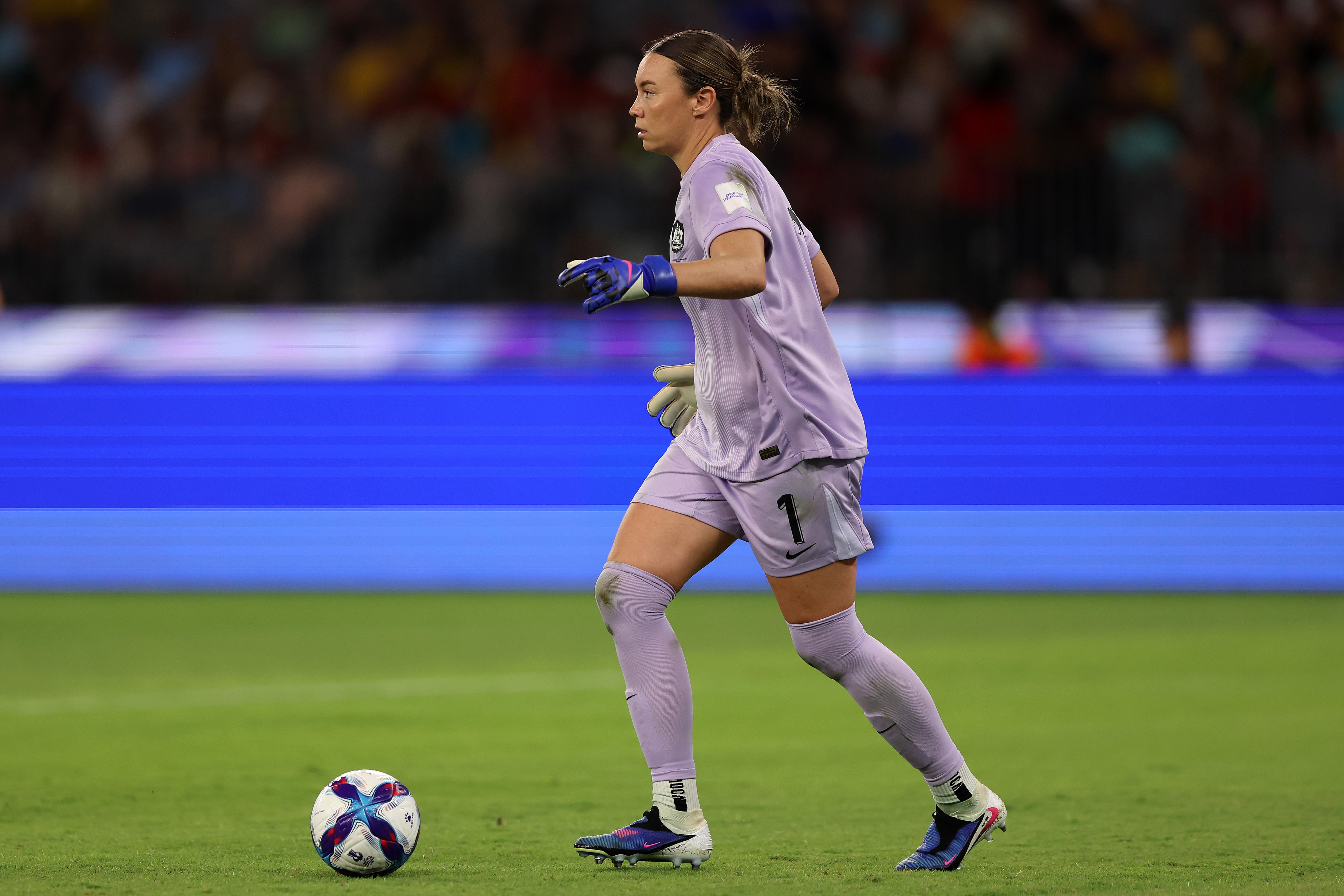 Um goleiro de cinza controla a bola em frente a painéis publicitários