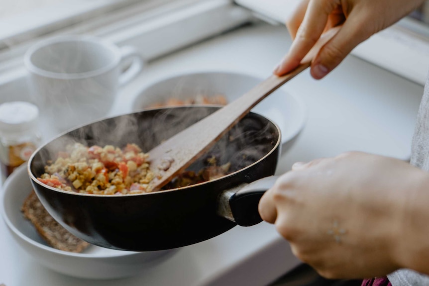 Close up of hands serving out a couscous dish from a frypan.