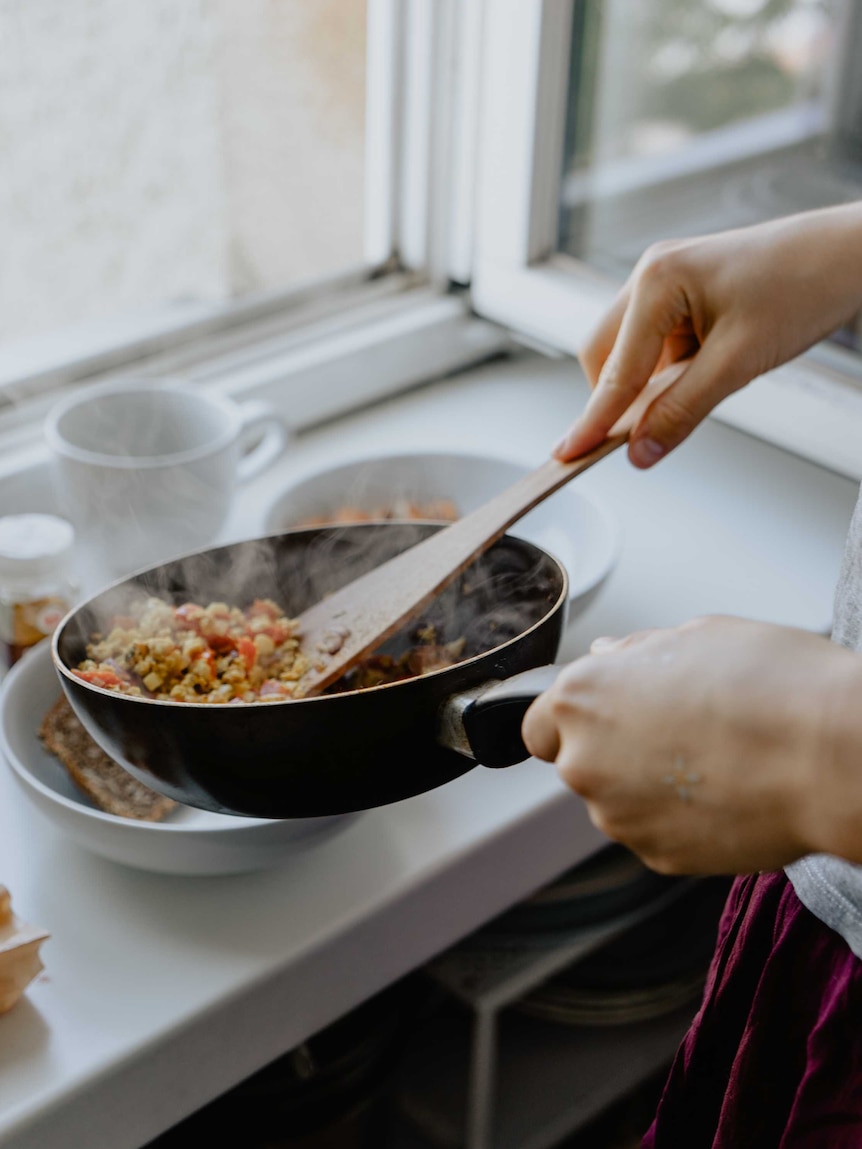 Close up of hands serving out a couscous dish from a frypan.