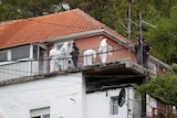 police and people in white protective suits stand on a deck outside a house where a shooting occurred
