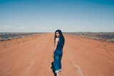 Fanny Lumsden walking away down a red dirt road, looking over her shoulder back towards the camera.