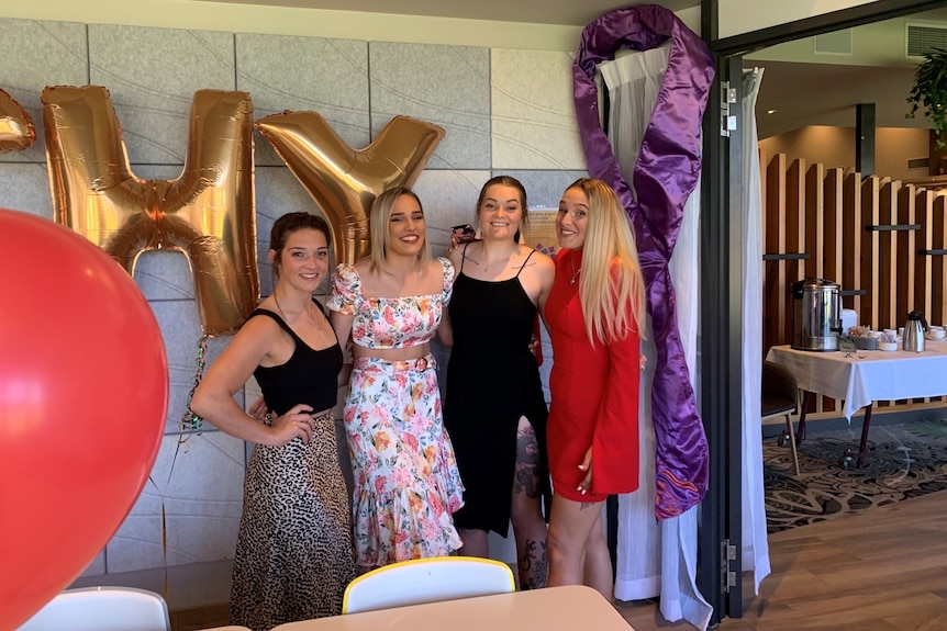 Four young women smile and pose for a photo at a function.