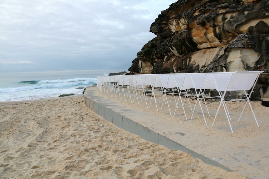 A sculpture at the base of a cliff overlooking a beach.