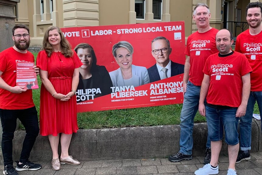 a group of five people wearing the colour red holding banners and flyers for the labor party