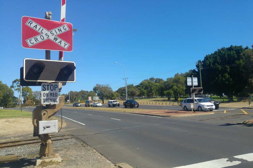 A railway crossing in Bunbury with signs and light signals on the side and in the middle of the road, and traffic oncoming.