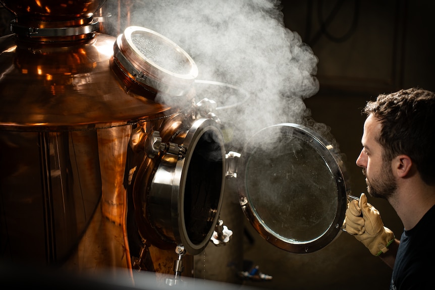 A man opens the door on a still and steam flows out of it